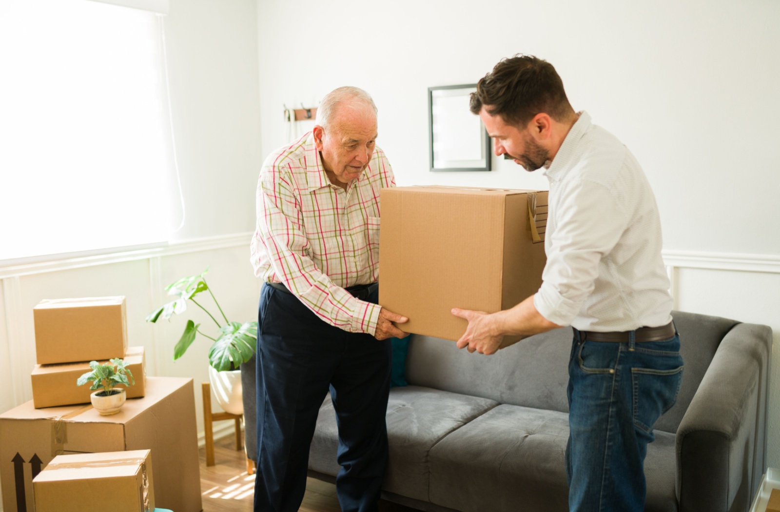 An adult child helping their older parent carry a box as they prepare for a move to assisted living.