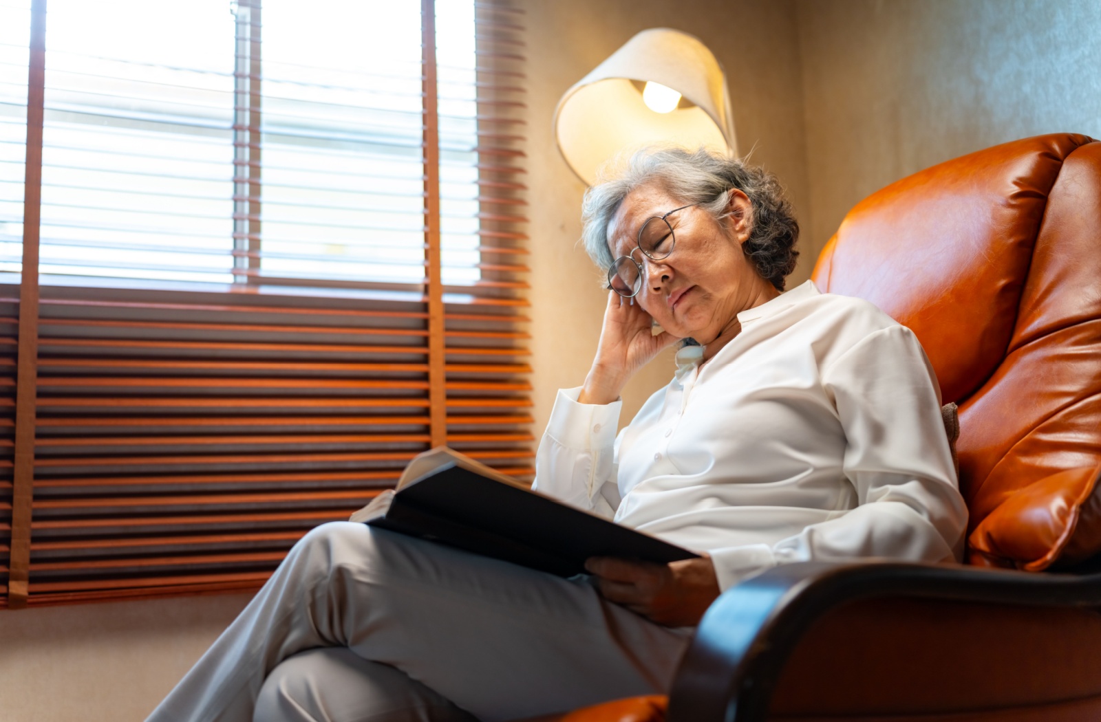 A senior dozes off while sitting and reading a book.