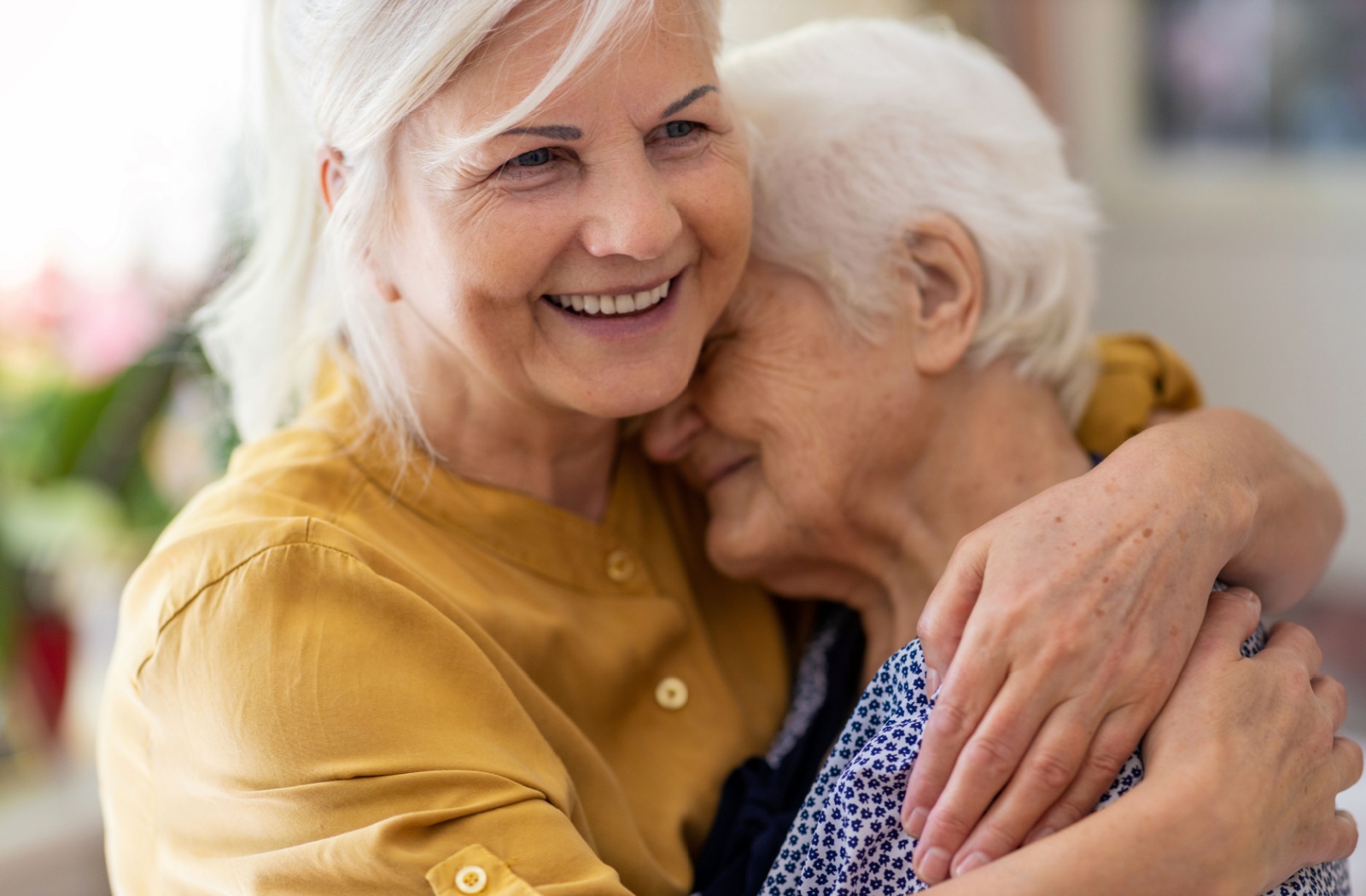 A close-up image of a smiling adult child hugging their older parent with dementia in memory care.
