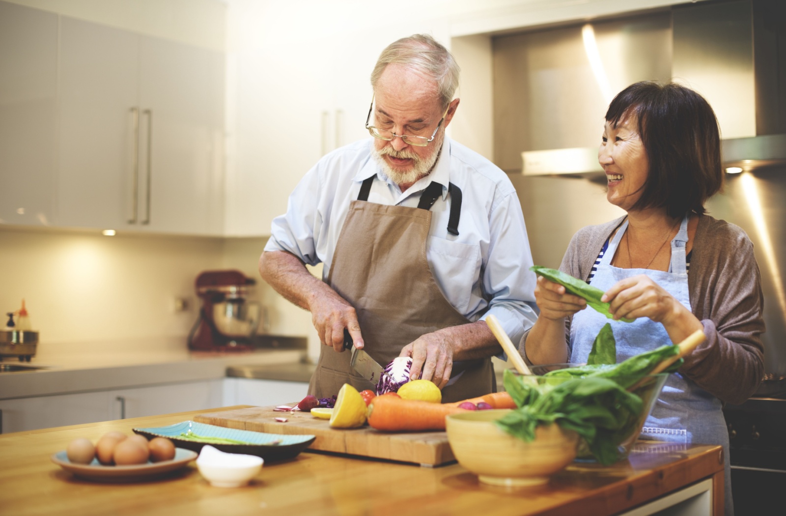 A senior couple chop vegetables together in the kitchen to prepare ingredients for making a hearty soup
