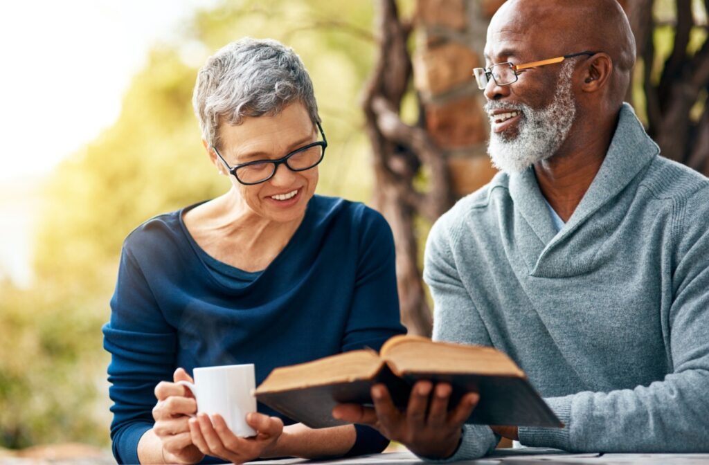 Two seniors smile as they read a book together over coffee.