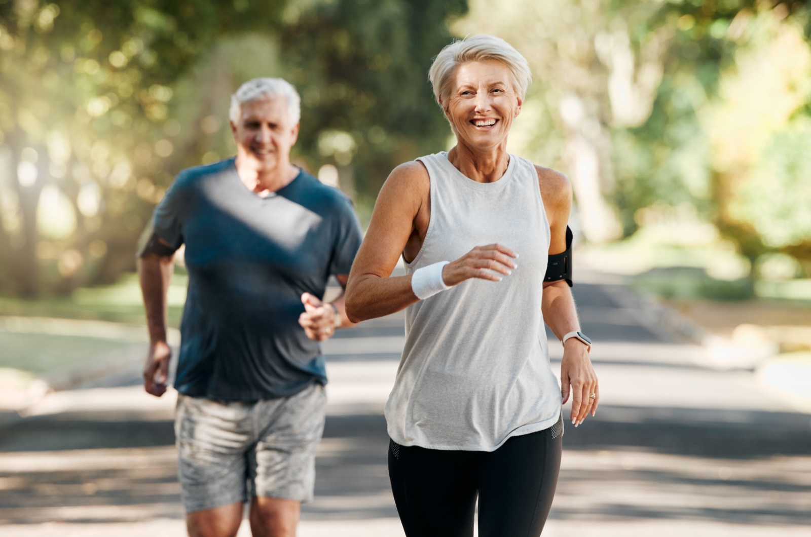 Two smiling older adults jogging outdoors.