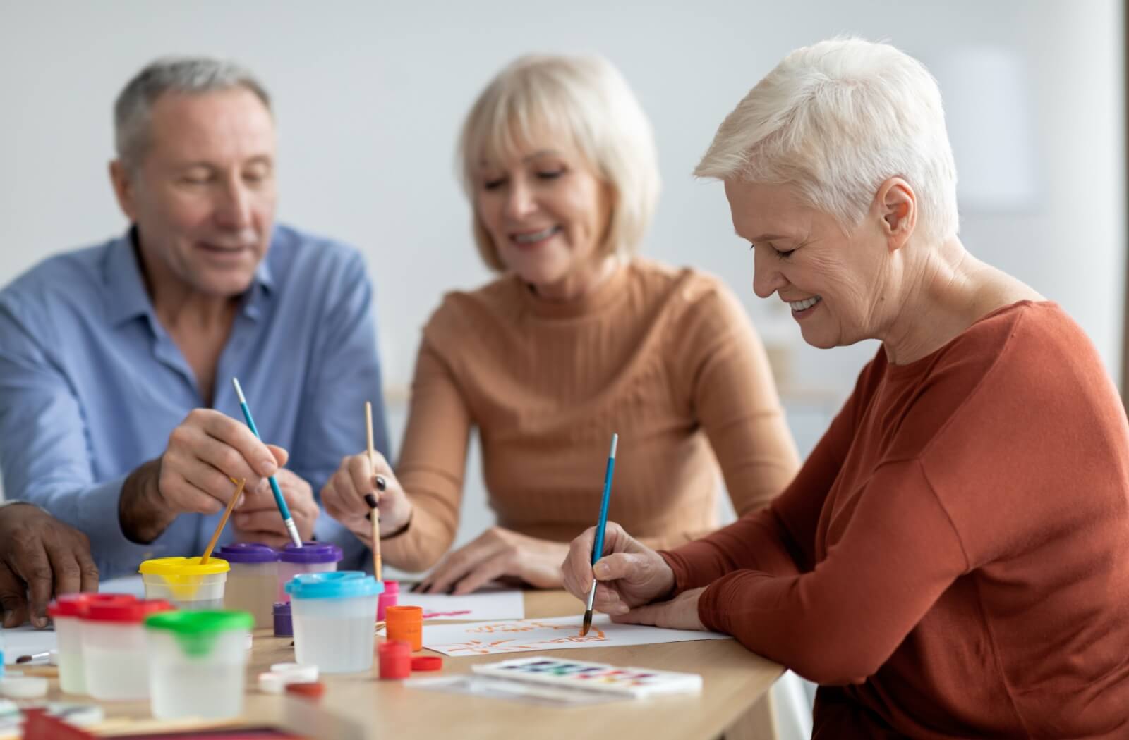 A group of older adults sitting at a table and enjoying painting.