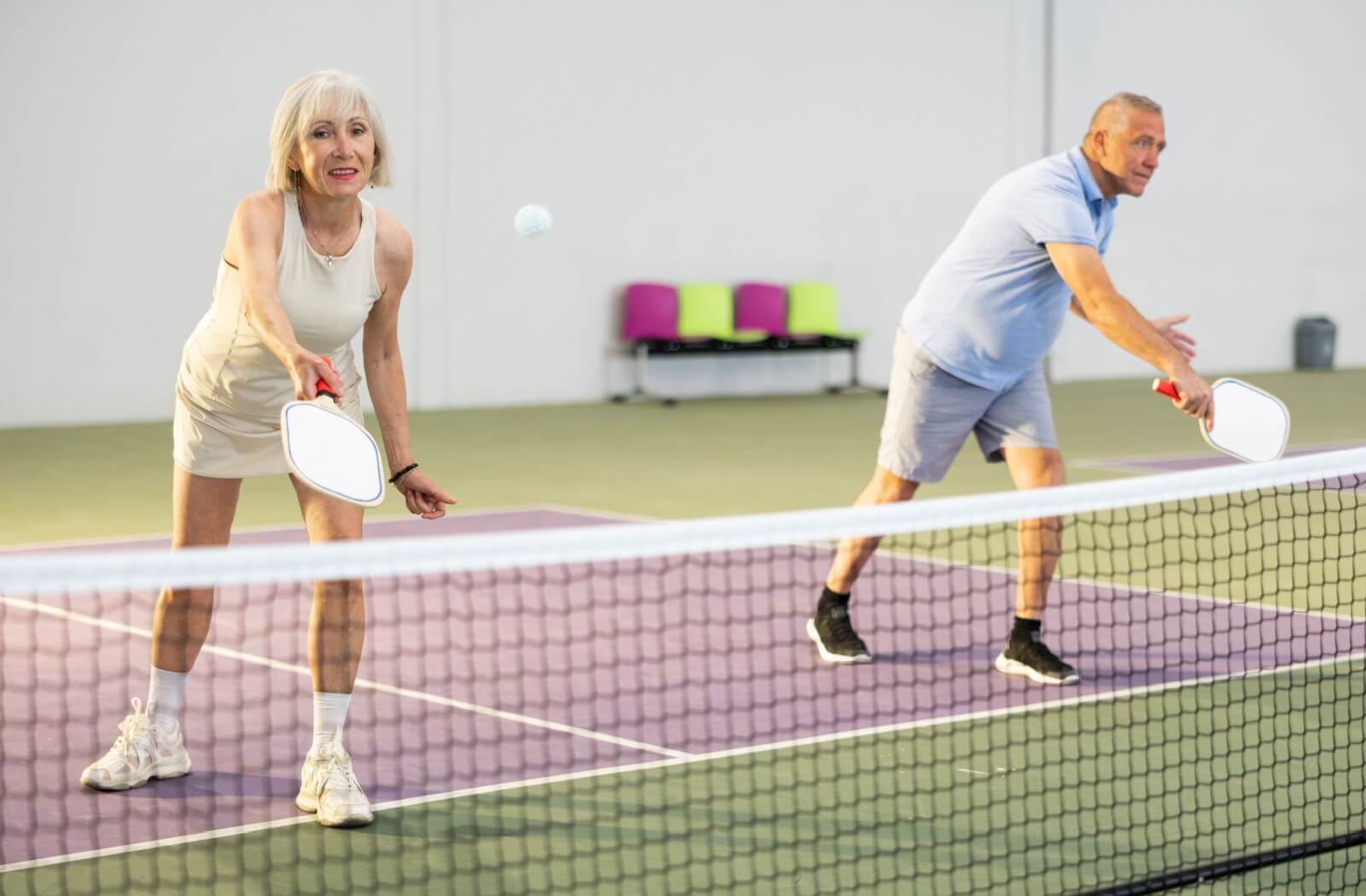 Two older adults holding pickleball paddles standing on one side of a pickleball court playing pickleball.