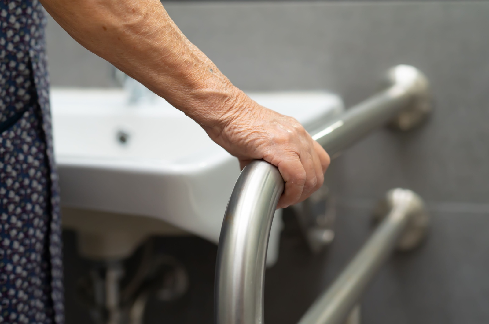 A close-up view of an older adult holding a grab bar with their right hand in the bathroom.