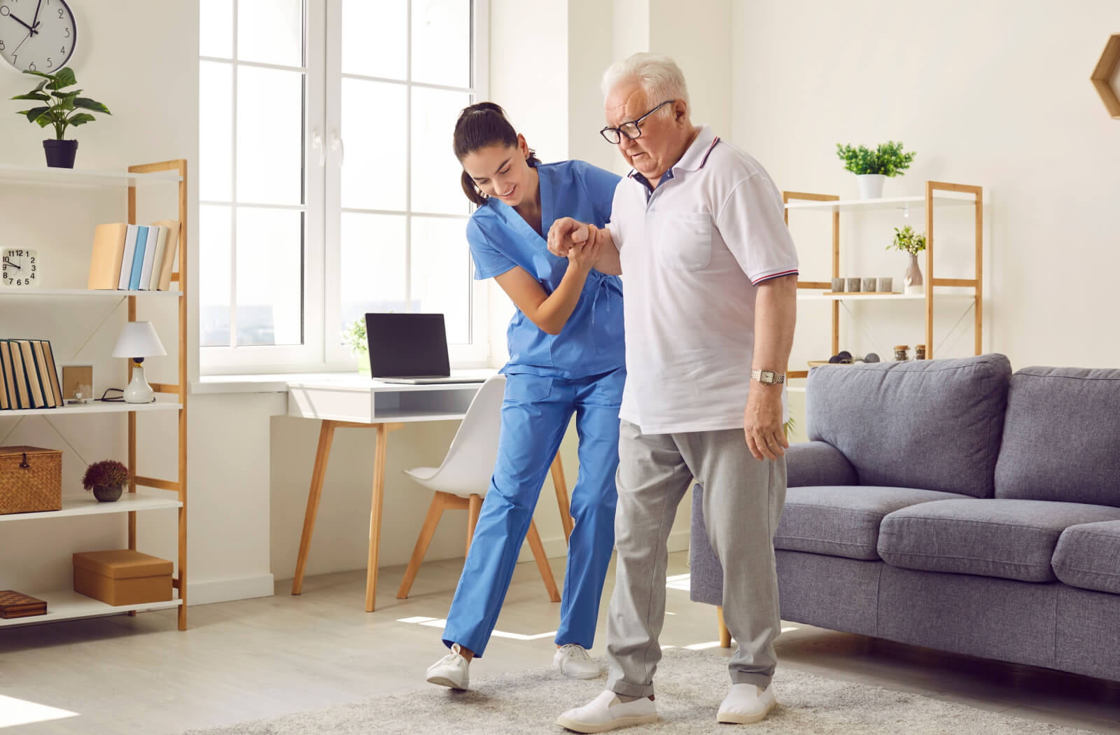 A caregiver helping an older adult walk across the living room due to their balance problems.