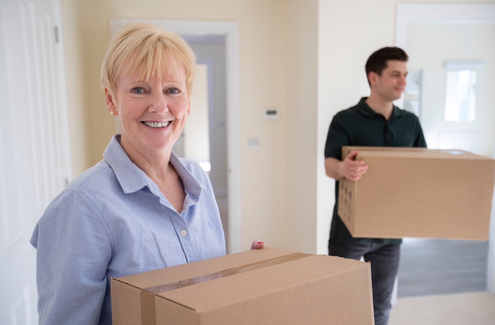 An older adult smiling and holding a box while their adult child helps them back to prepare for assisted living.